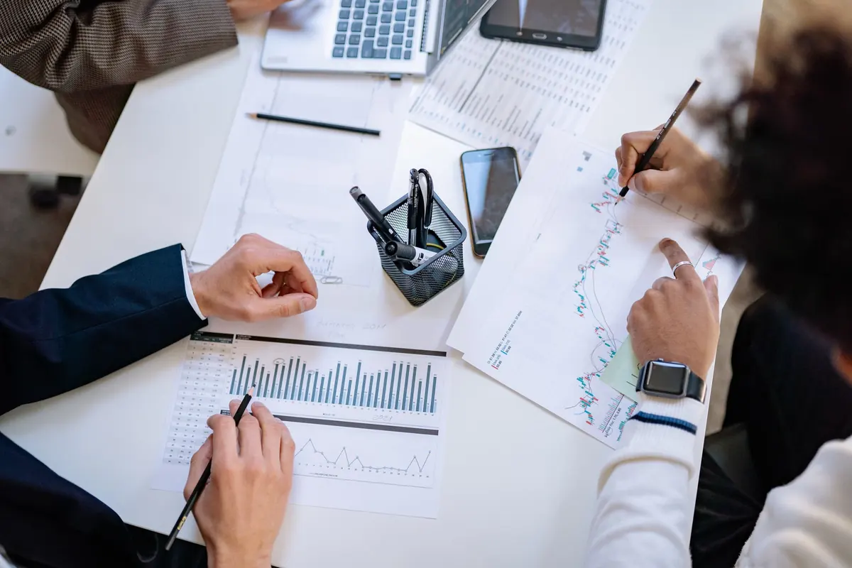 Manos que comparan gráficas impresas alrededor de una mesa