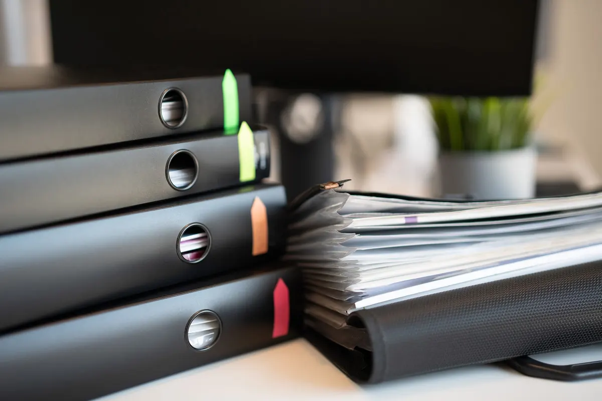 Archivadores oscuros con etiquetas de colores junto a documentos sobre un escritorio