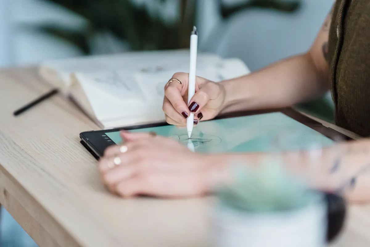 Manos que dibujan con un lápiz digital en una tableta sobre una mesa