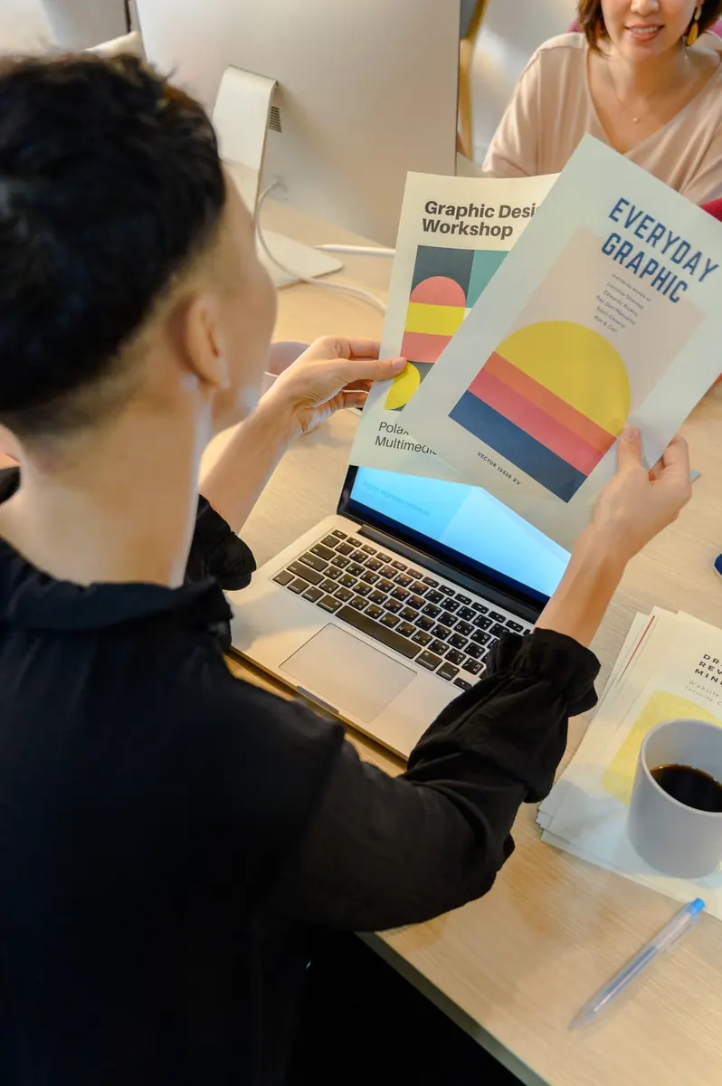 Personas que consultan libros de diseño gráfico junto a un portátil