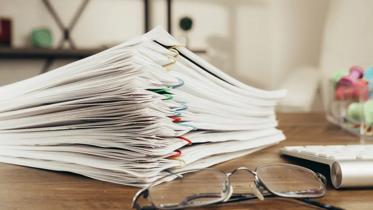 Pila de documentos sujetos con clips junto a unas gafas sobre una mesa