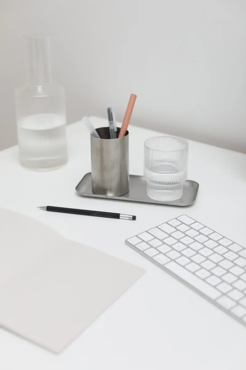 Teclado, cuaderno, lápices y vaso de agua sobre un escritorio blanco