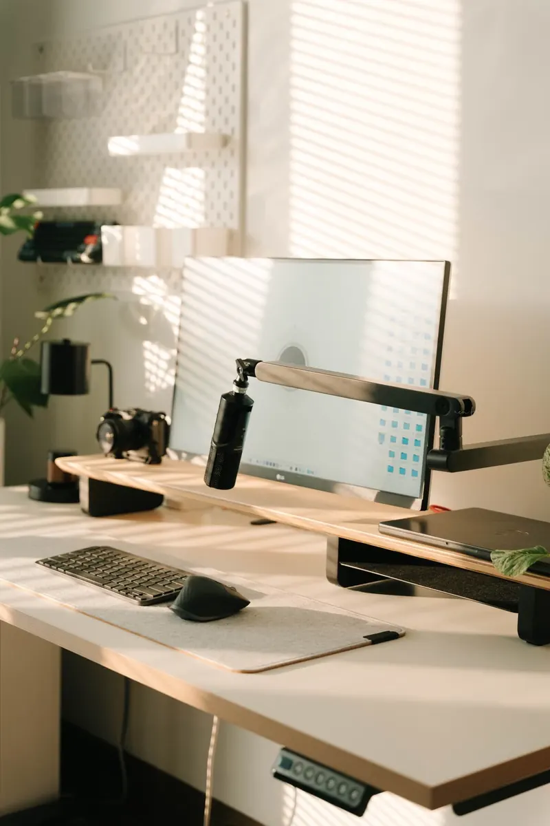 Monitor, teclado y micrófono en un escritorio iluminado por una ventana