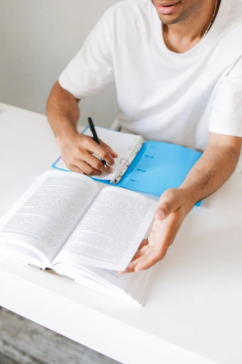 Persona que escribe apuntes mientras consulta un libro abierto