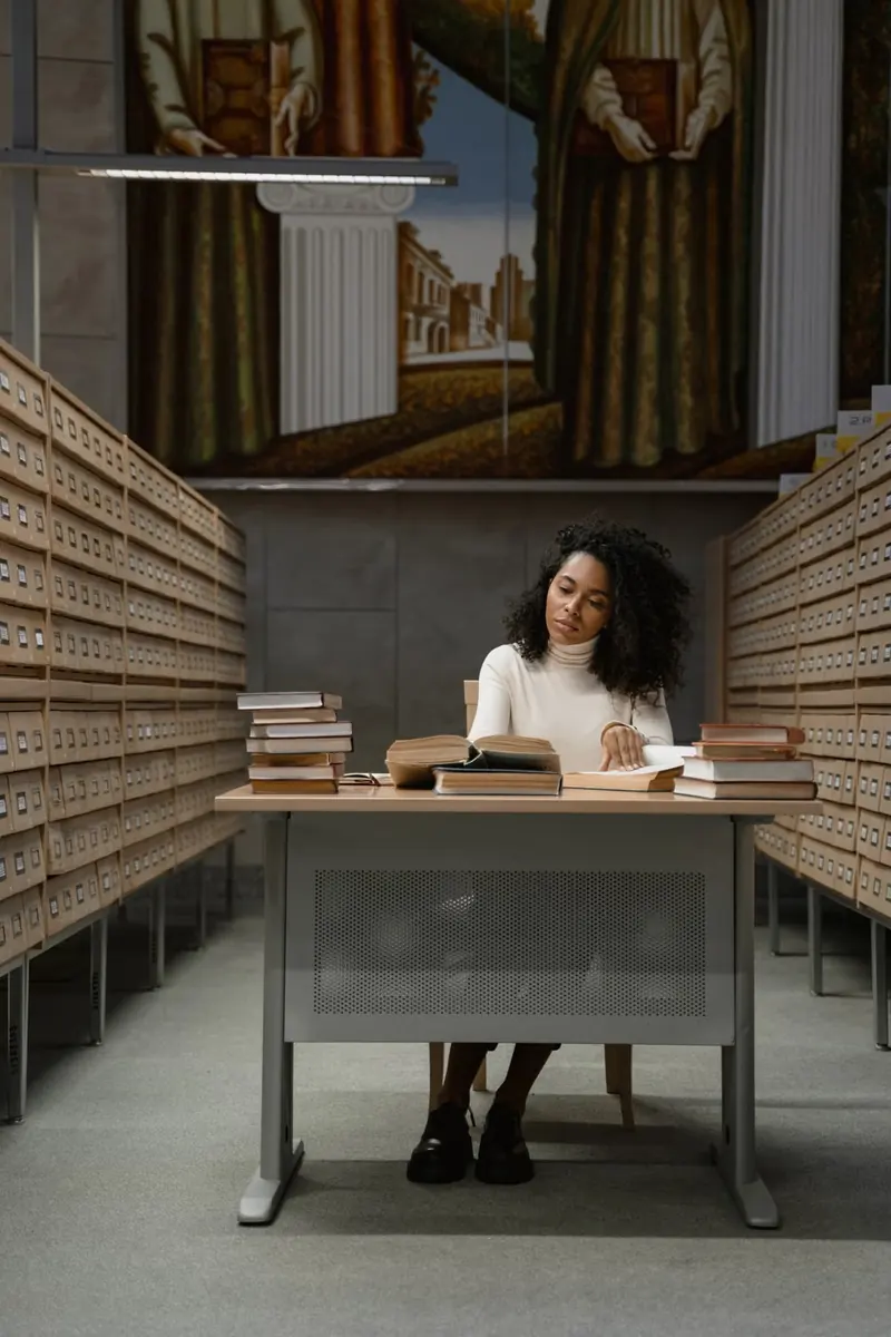 Persona que lee en una mesa rodeada de libros y archivos