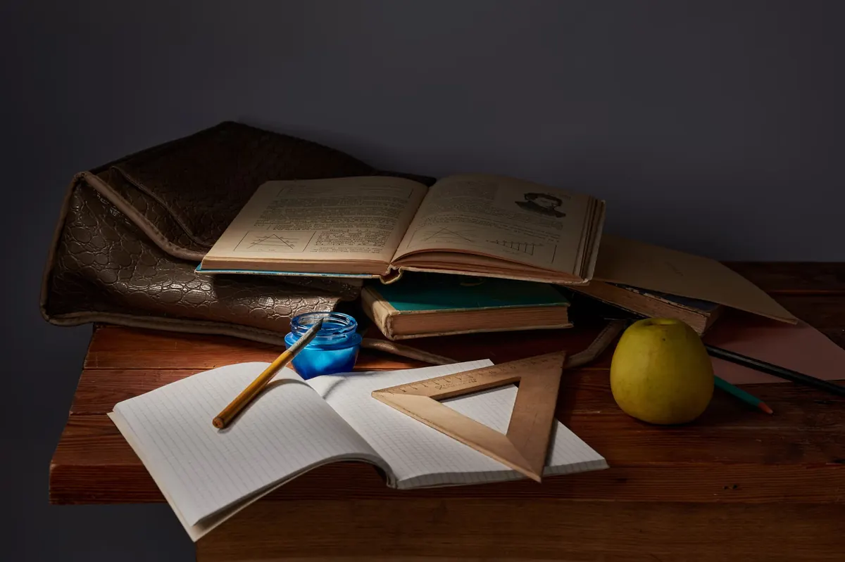 Libros, cuaderno, regla y lápices sobre una mesa con una manzana y un maletín