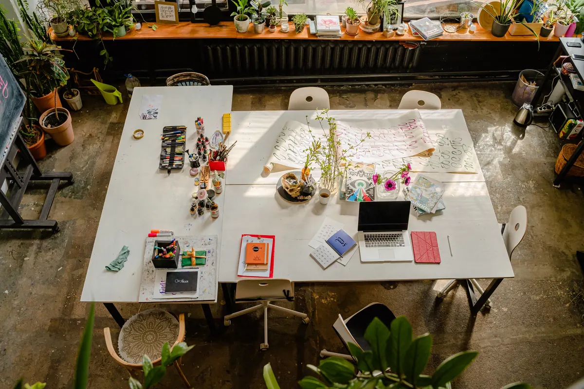 Vista superior de una mesa compartida con materiales de dibujo, portátil y plantas