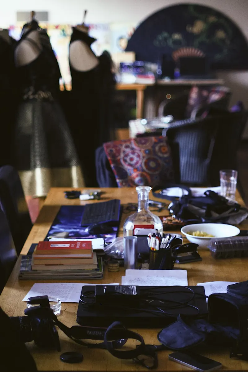 Mesa de un taller de costura con materiales, máquina de coser y maniquíes al fondo