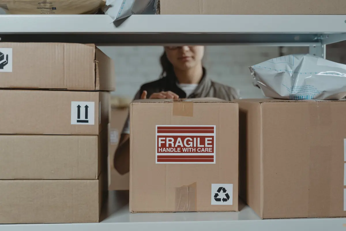 Persona que organiza cajas con etiquetas de manejo en un almacén