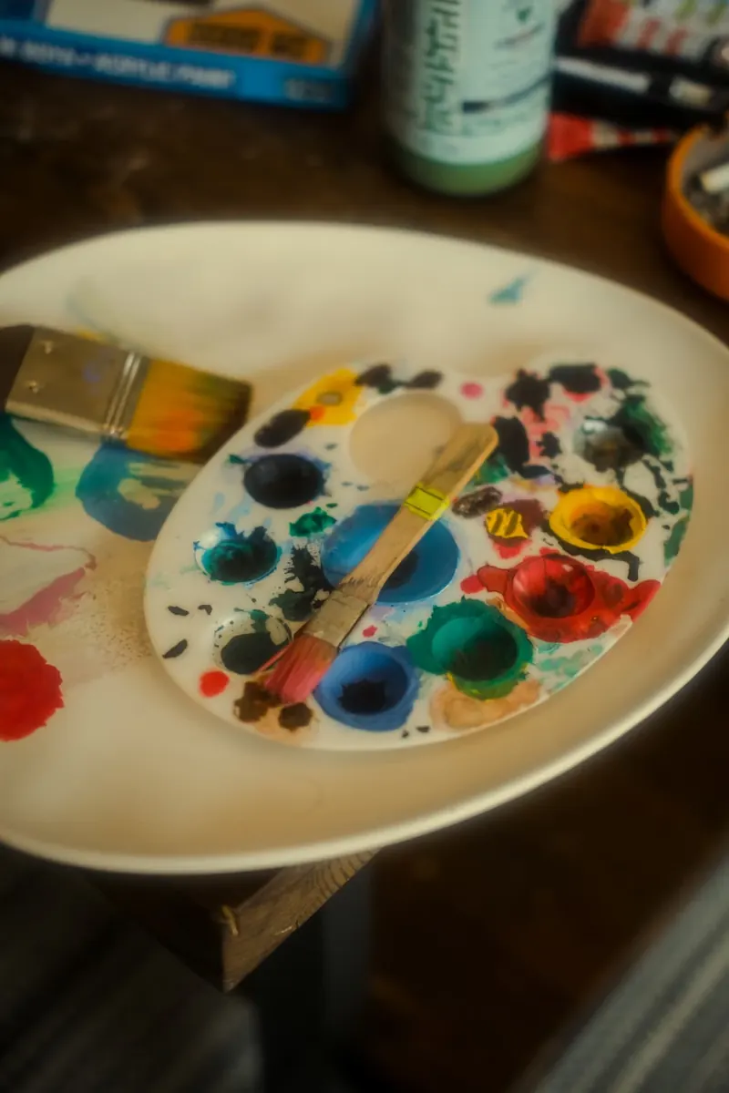 Paleta con pinturas de varios colores y pinceles sobre una silla