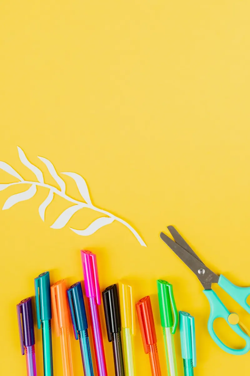 Rotuladores, tijeras y recortes de papel sobre un fondo amarillo