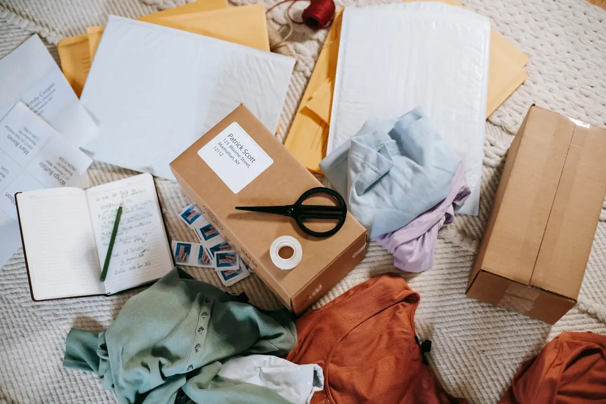 Cajas, sobres, ropa, tijeras y cuaderno organizados sobre una superficie clara