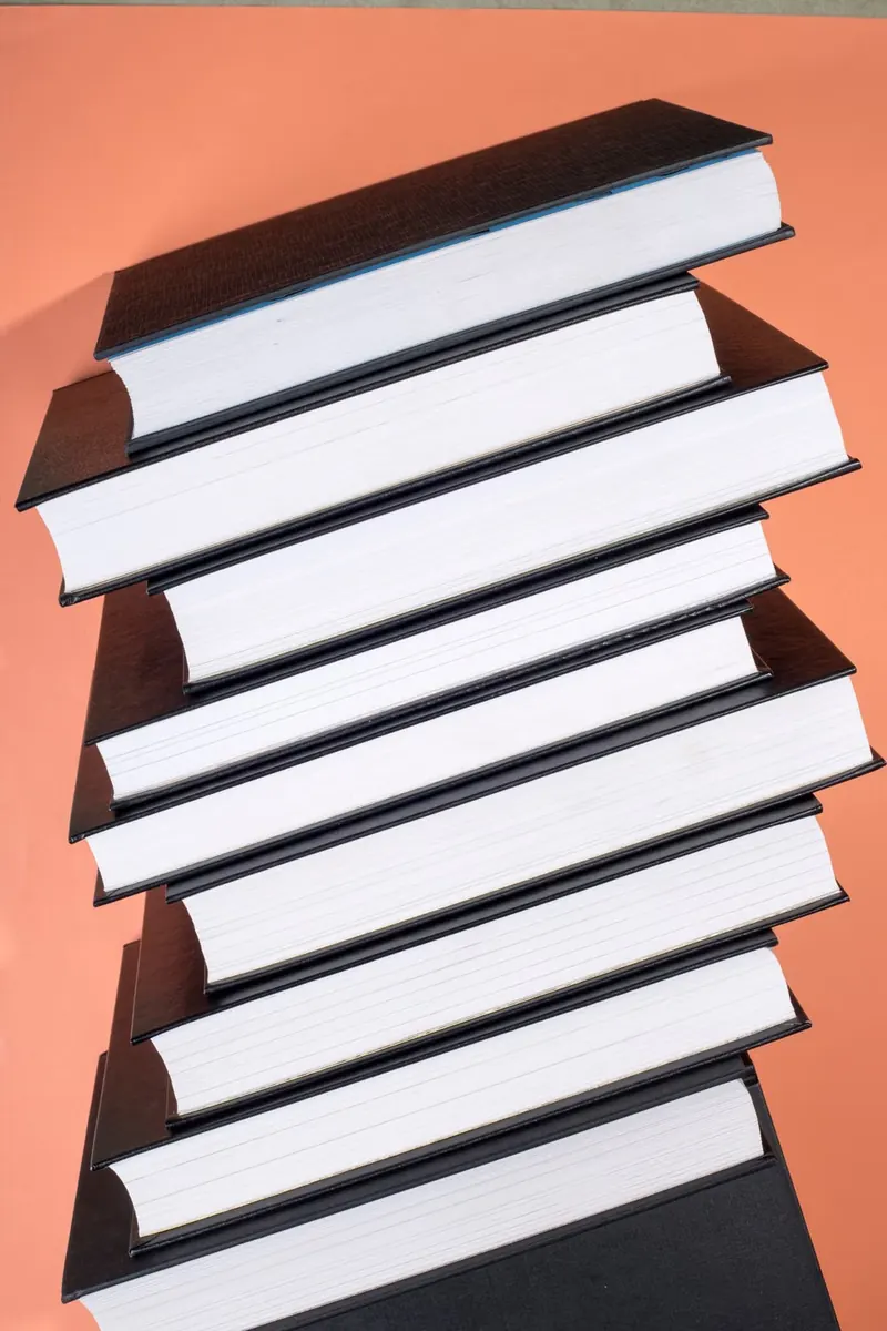 Pila inclinada de libros de tapa negra sobre un fondo color durazno