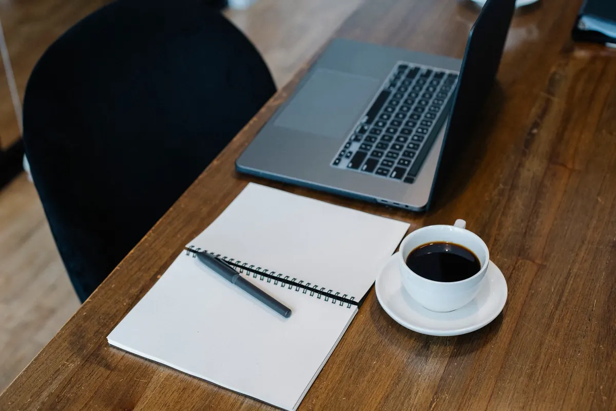 Portátil, cuaderno abierto y taza de café sobre una mesa de madera
