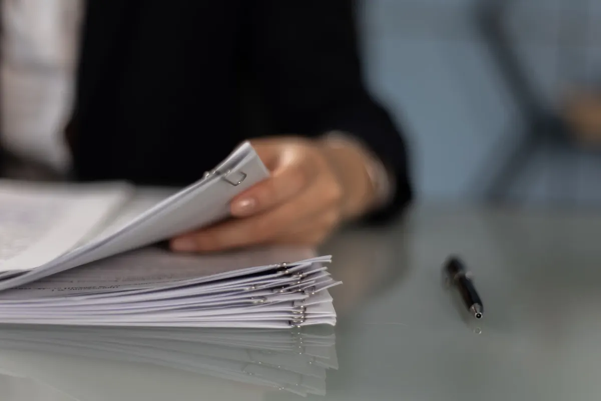 Mano que sostiene varias hojas sobre una pila de documentos