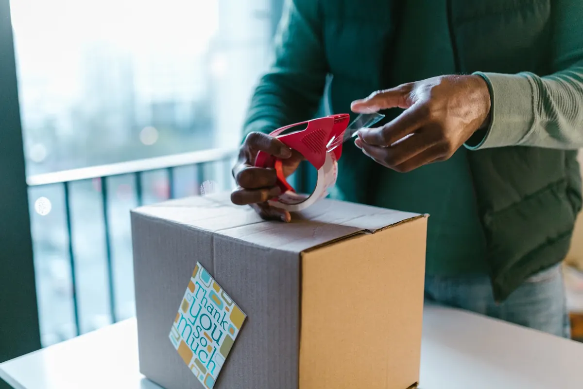 Manos que sellan una caja de cartón con un dispensador de cinta