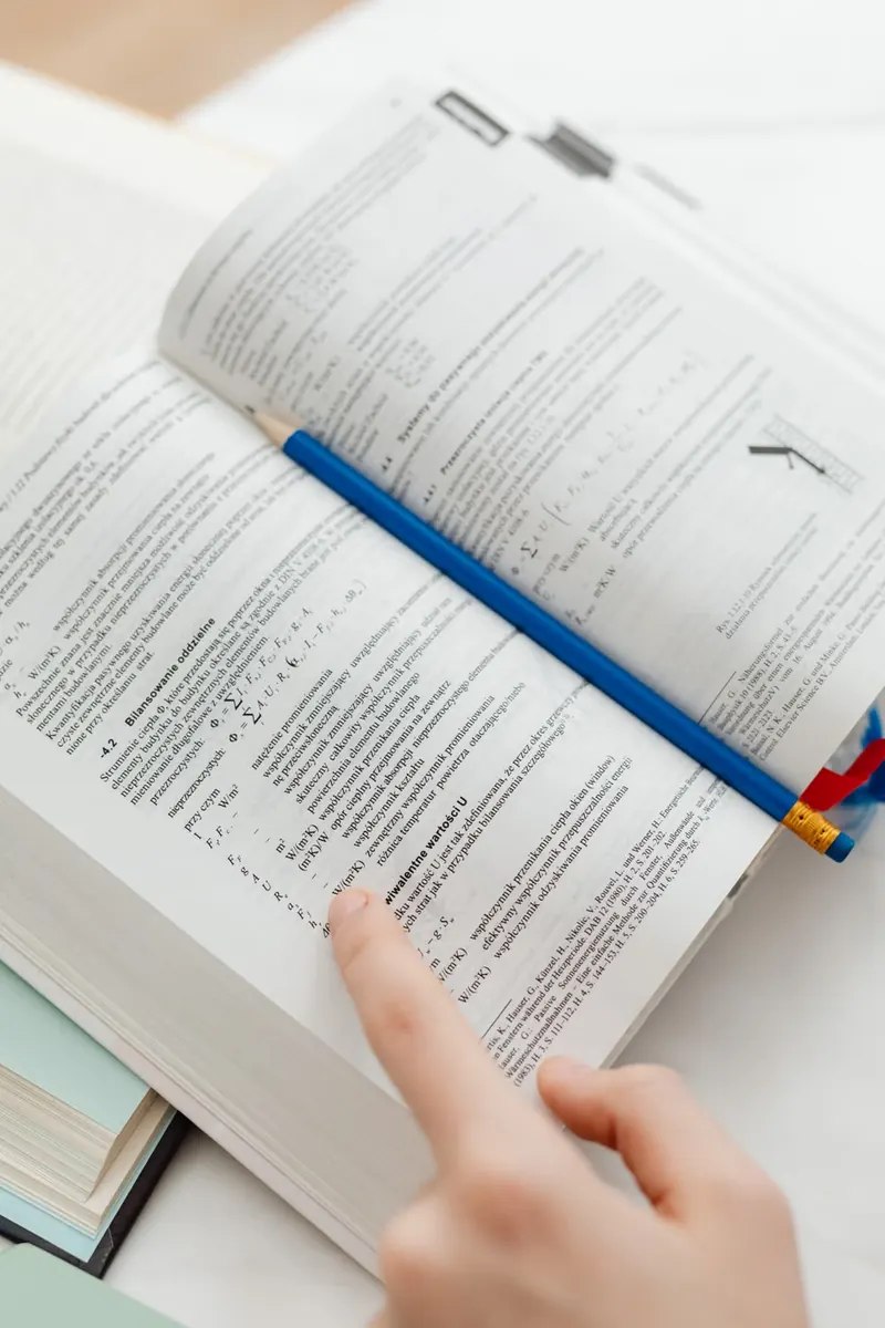 Mano que señala un texto en un libro abierto junto a un lápiz azul